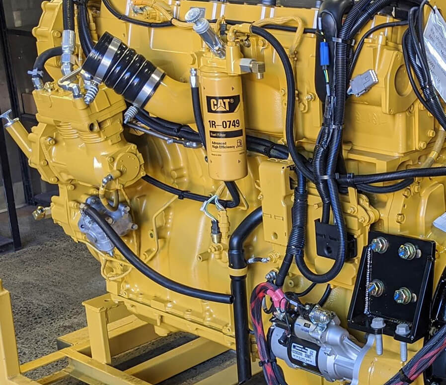 Close-up of a yellow CAT diesel engine with visible hoses, wiring, and fuel filter components.