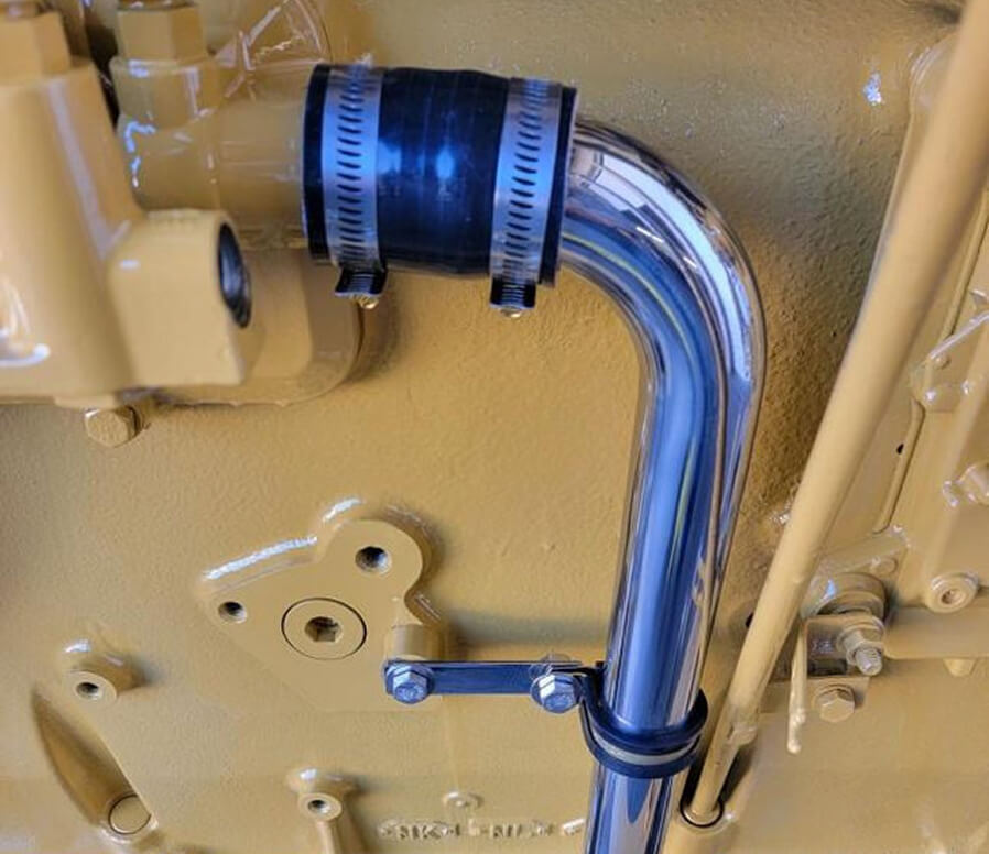 Close-up of a chrome metal pipe with rubber coupler mounted on a yellow engine block.