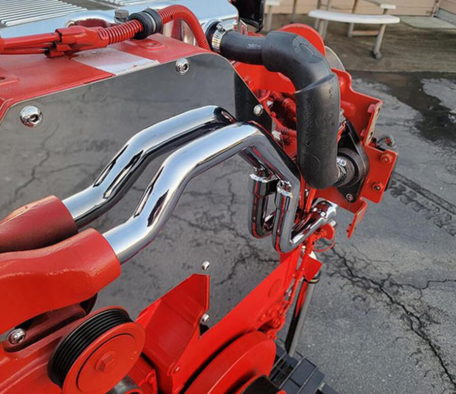 Close-up of polished chrome exhaust pipes and black intake tubing on a red industrial engine.