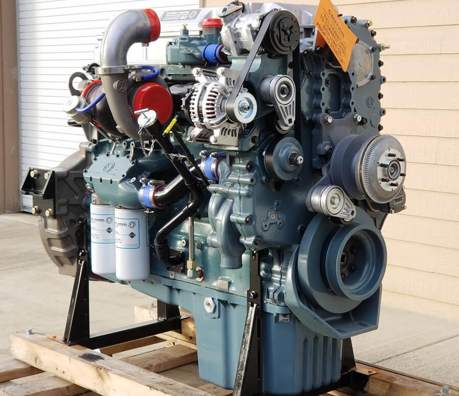Large industrial diesel engine mounted on a wooden pallet with visible belts, pulleys, turbocharger, and filters.