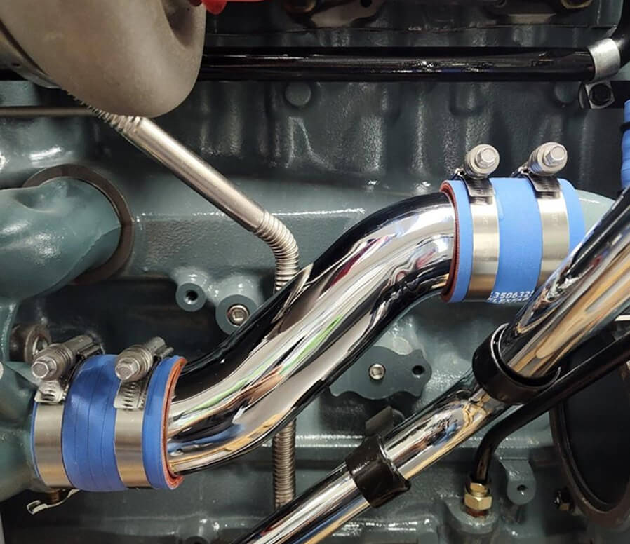 Close-up of polished chrome engine piping secured with blue silicone couplers and metal clamps on a diesel engine.