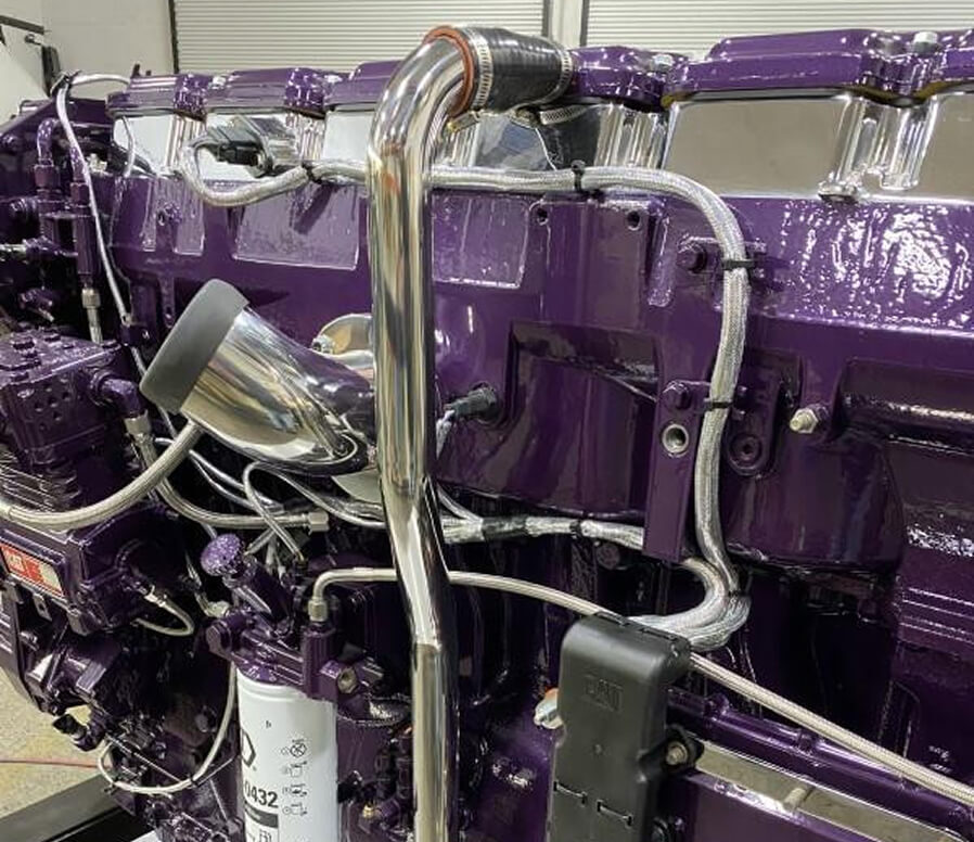Close-up of a custom-painted purple diesel engine with polished chrome piping and braided lines.